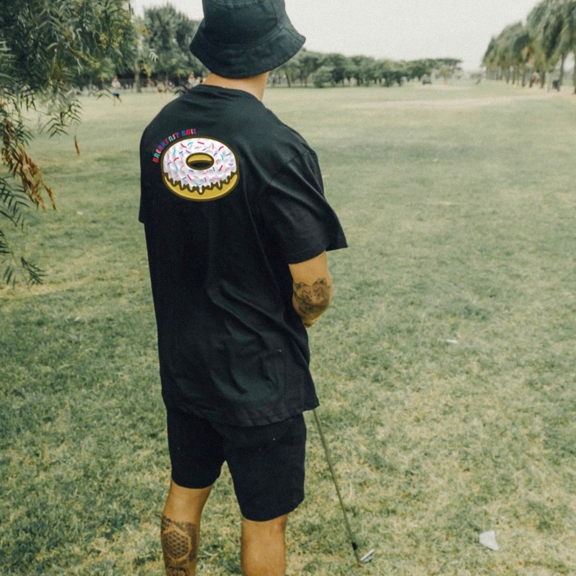 man on golf course holding a golf club wearing the black breakfastball shirt.  