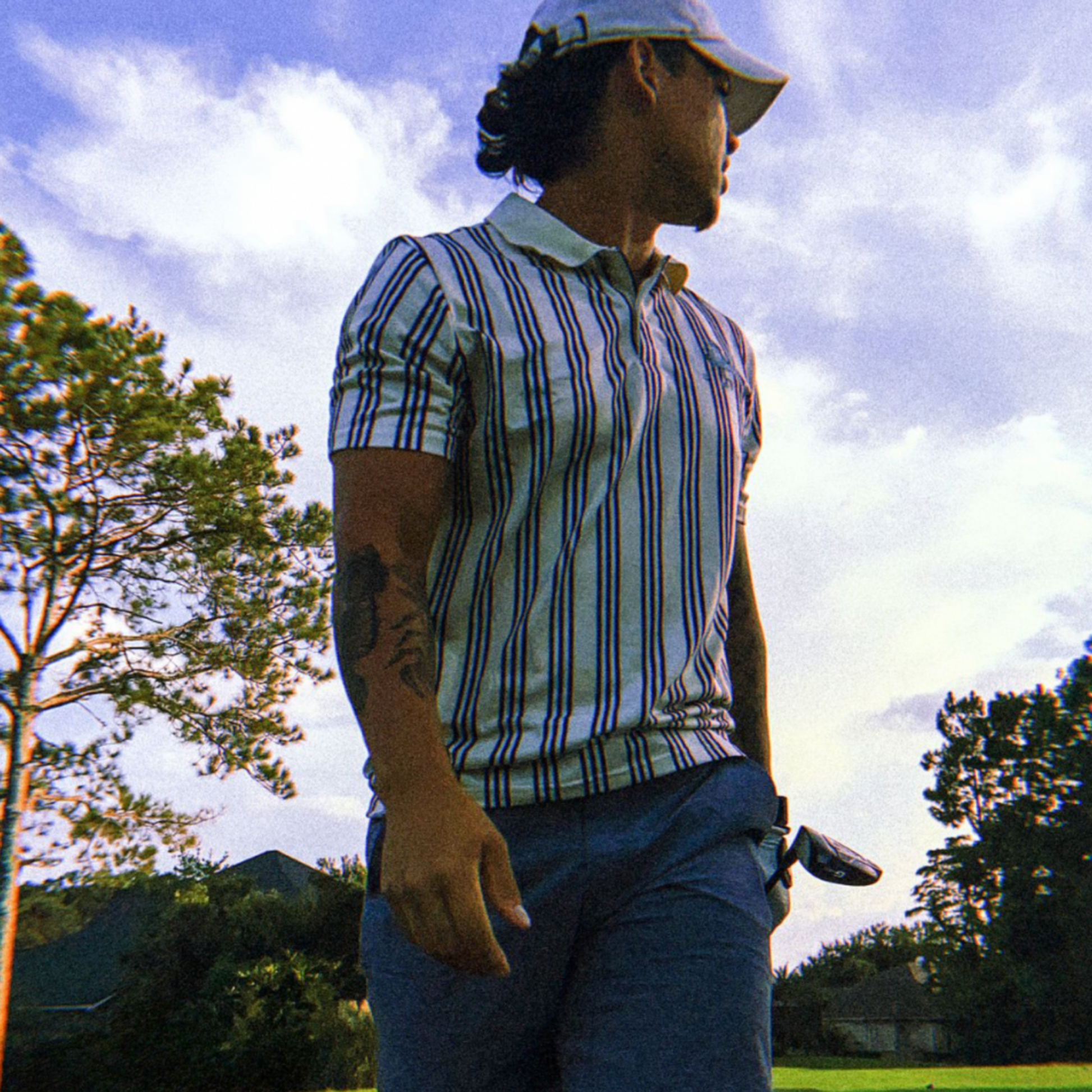 man holding a golf club wearing the og unisex stripped polo.  Walking away from his tee shot. 